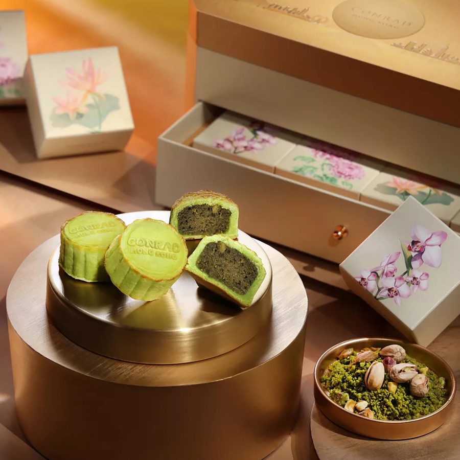 Product image of Conrad Hong Kong’s Mini Pistachio Mooncakes, showcasing the mooncakes, ingredients and floral packaging against a gold surface. 