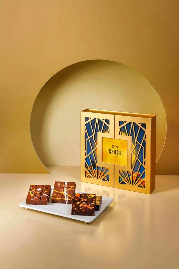 Product image of Dalloyau’s DA CHOCO Golden Autumn Crispy Chocolate, with chocolates placed on a white plate in front of the gold packaging.