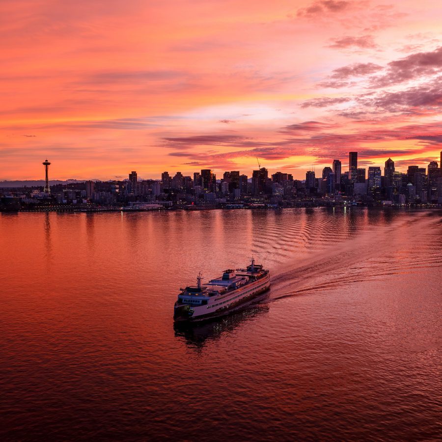 A ferry sails across the water in Seattle with a view of the sunset skyline in the background.