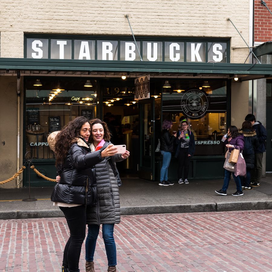 Two women stand outside Starbucks taking a selfie in Seattle.