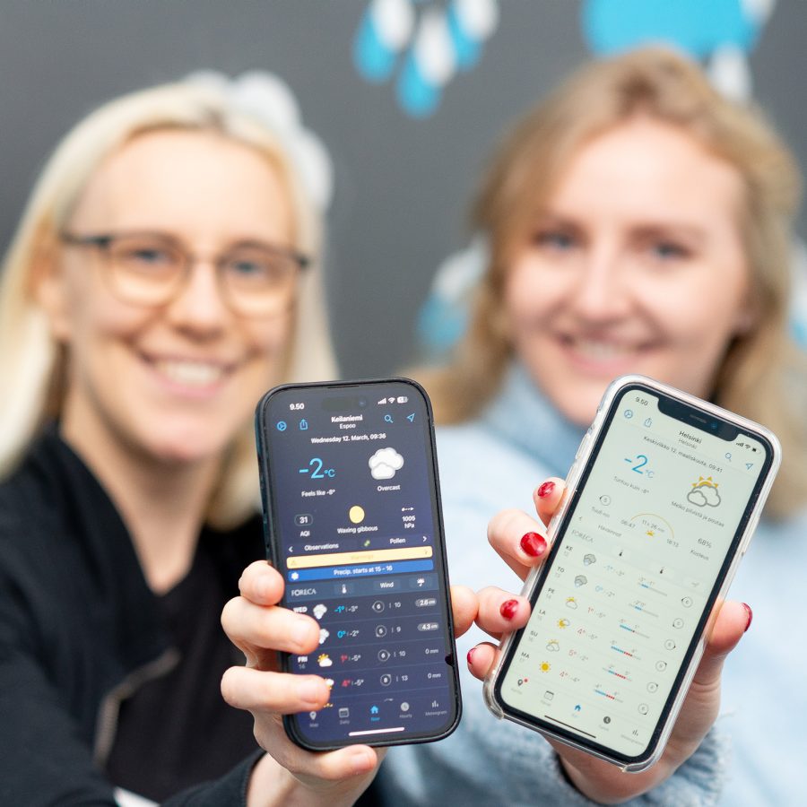 Two women holding up two smartphones with wearther app Foreca shown on the screen.