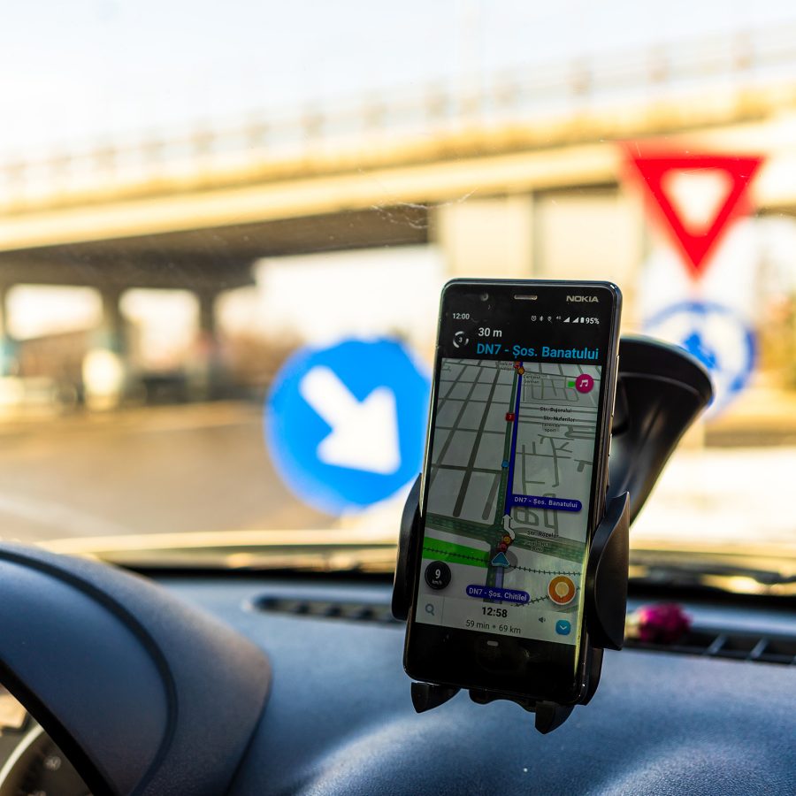 A smartphone on a car mount inside a vehicle with Waze app on the screen and a view of a road seen through the windshield.