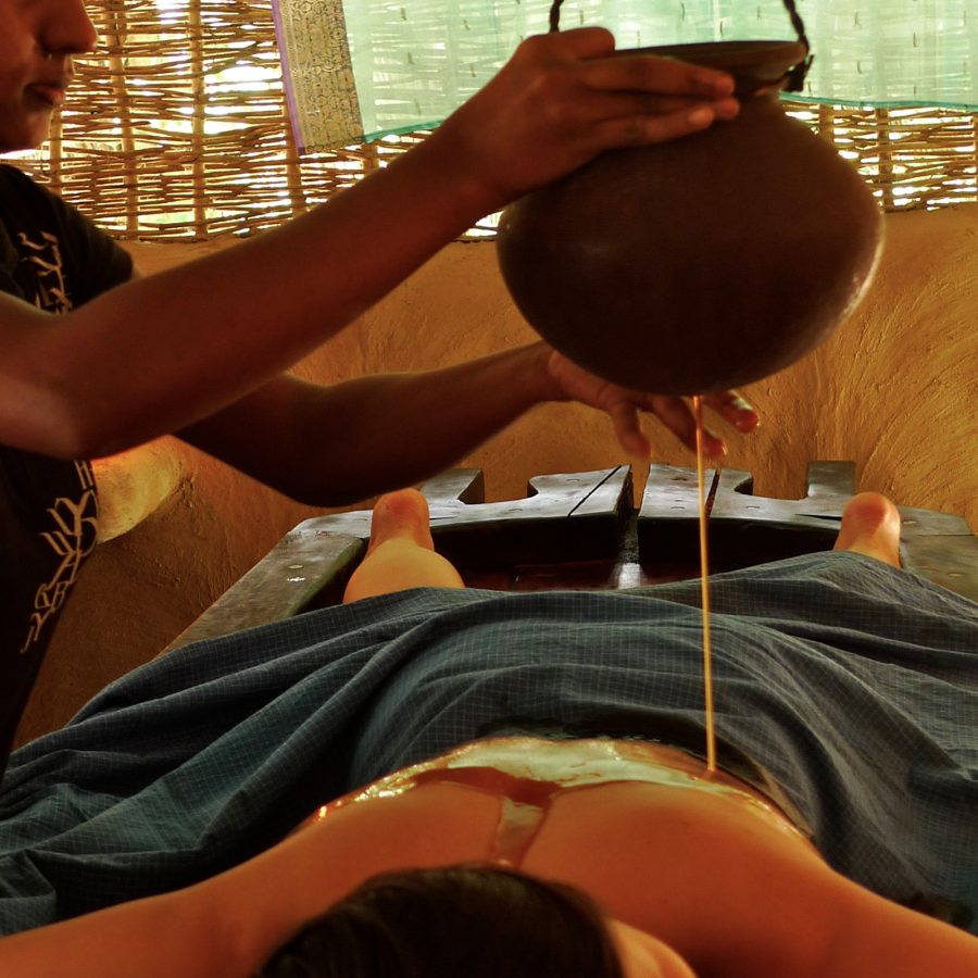 Person pouring oil onto another person’’s back during a massage.