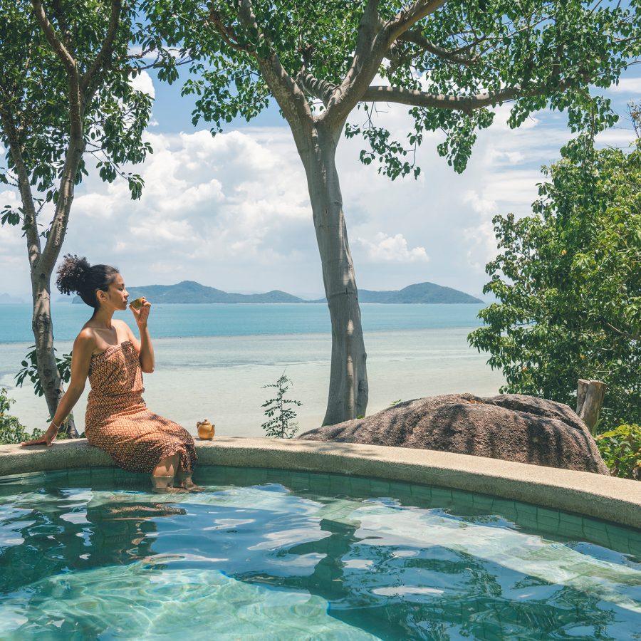 A woman sits on the poolside looking out at the beach at Kamalaya Koh Samui. 