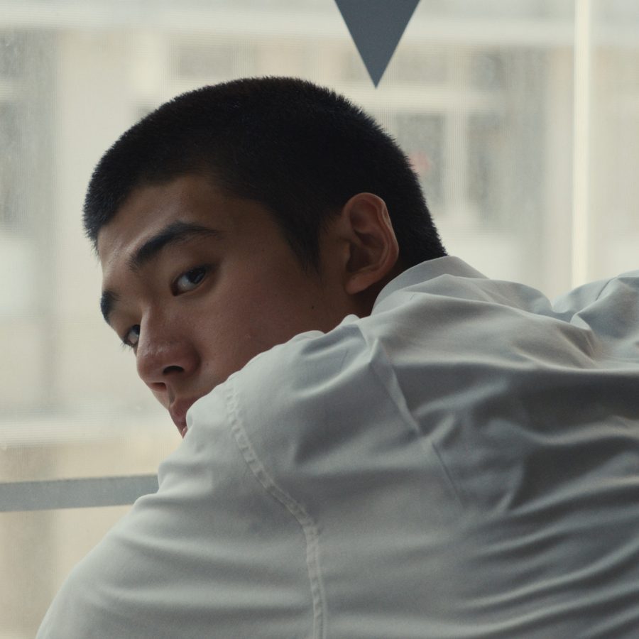 A teenage boy sits pensively near a window in a scene from HAPPYEND.