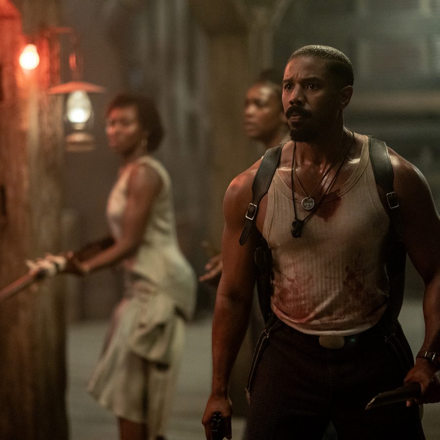 In a dim room, a group of people stand poised with weapons in a scene from Sinners.