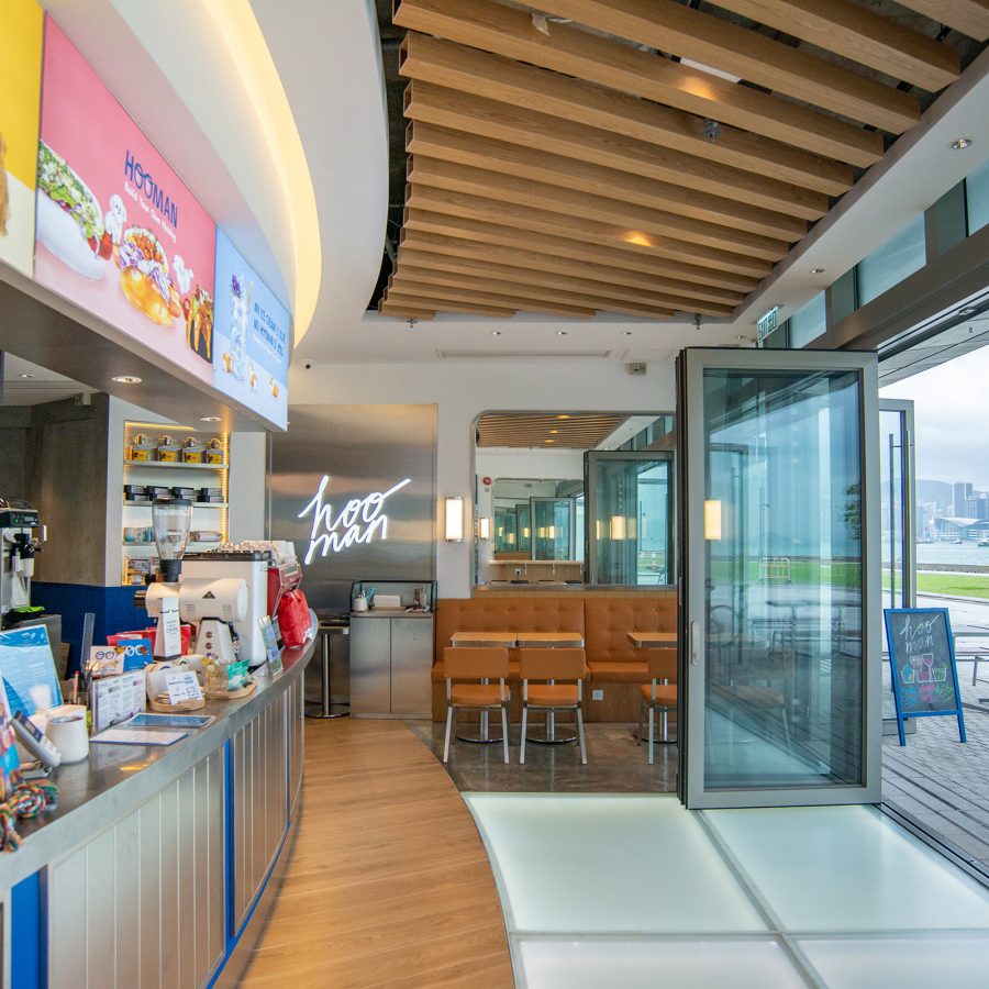 An interior view of Hooman by the Sea shows the shop’s colourful overhead menu above the bar, which looks out at the West Kowloon Waterfront Promenade.