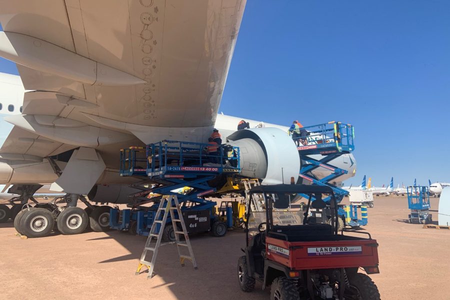 Workers on scissor lifts maintaining a Cathay Pacific airplane engine with other aircraft in view.