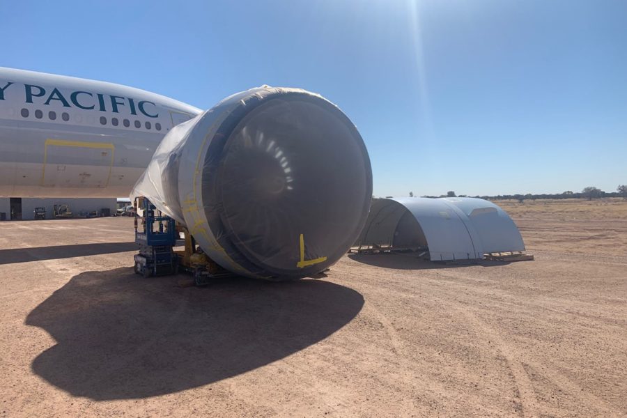 Cathay Pacific aircraft with engine wrapped in plastic, parked on dirt under clear sky.
