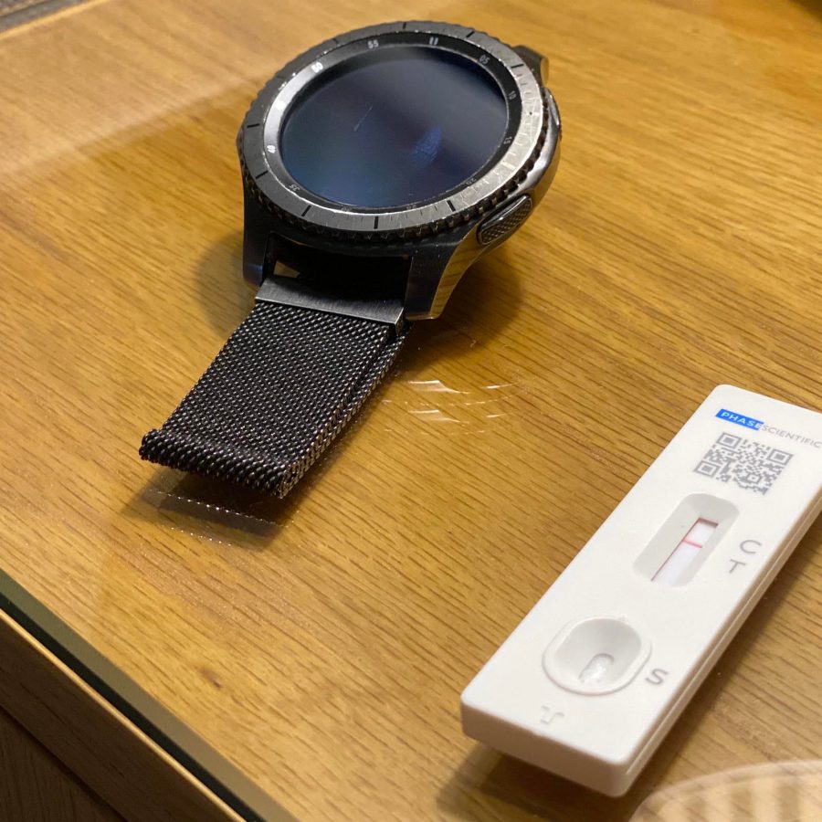 Smartwatch next to a COVID-19 rapid test showing a faint positive result.