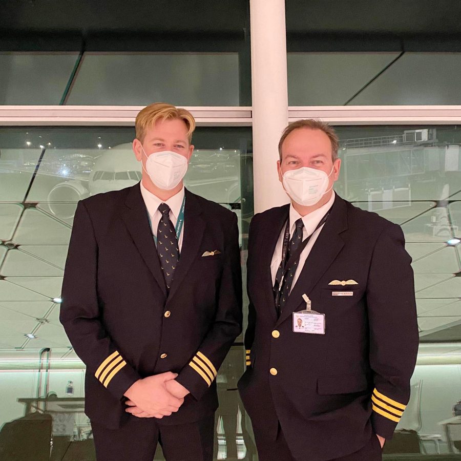 Two airline pilots in uniform and face masks standing in an airport terminal.