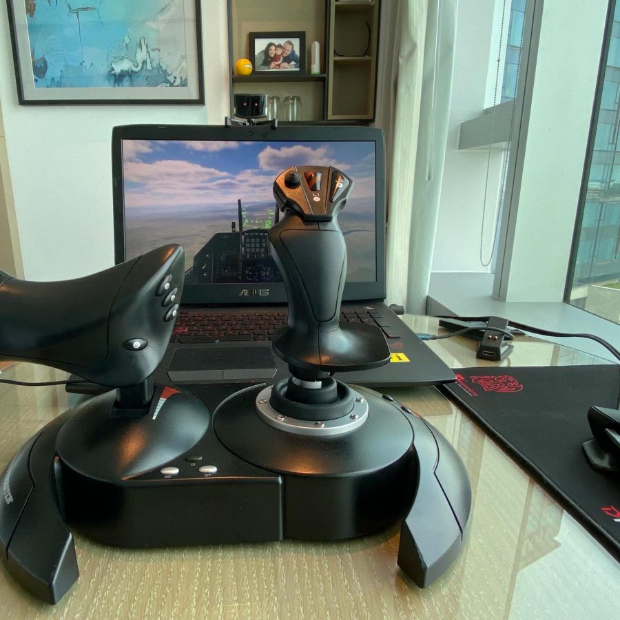 A flight simulator setup on a glass table with a joystick and throttle in front of a laptop displaying an aircraft cockpit view. 