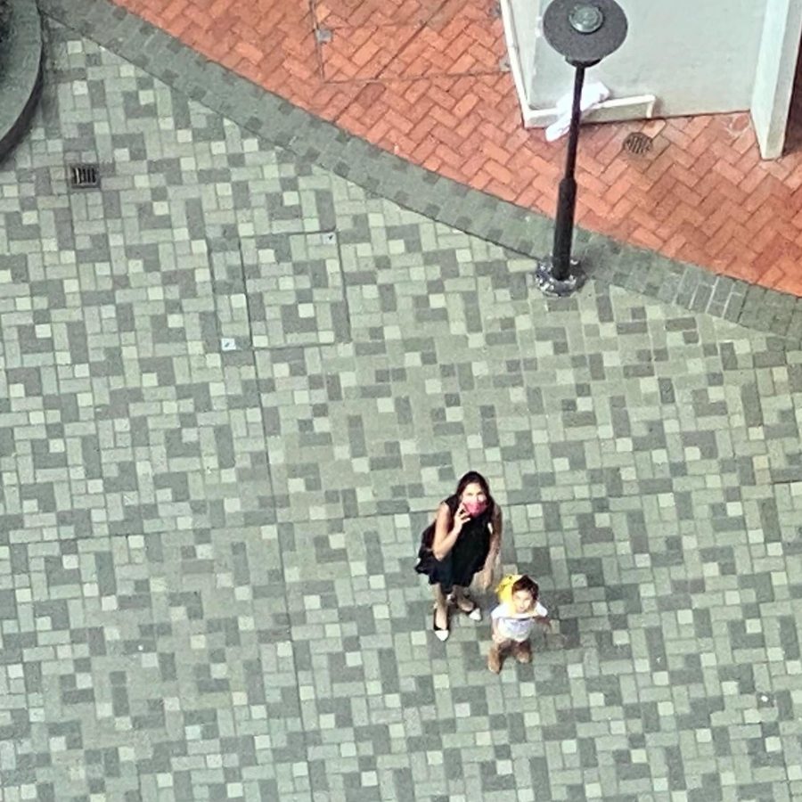 Aerial view of an adult and child standing on a tiled outdoor plaza.