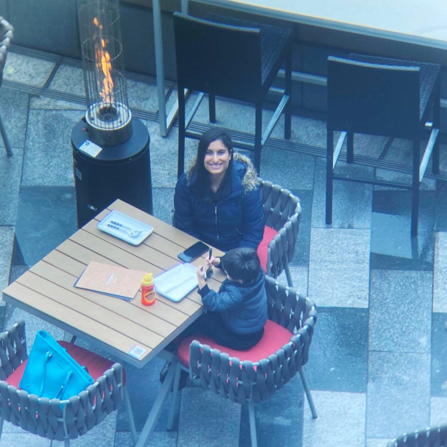 Top-down view of two people seated at an outdoor table with food items and a heater nearby.