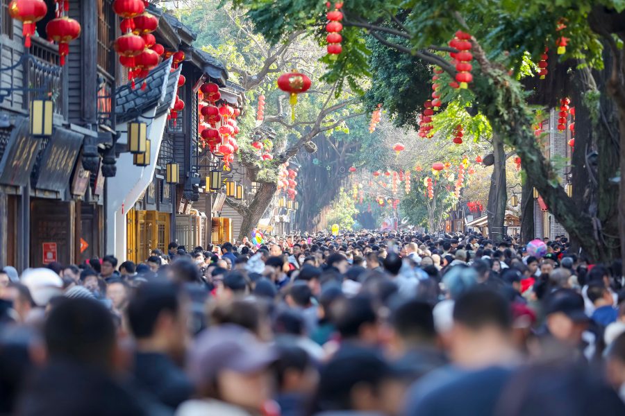 A crowd of people walking down a street with traditional Chinese buildings, lanterns and trees in Fuzhou’s Sanfang Qixiang. 