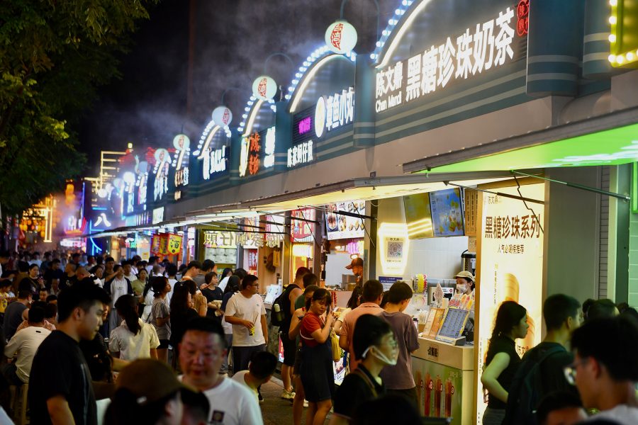Lots of people standing around a row of lit-up food stalls in Sanfang Qixiang.
