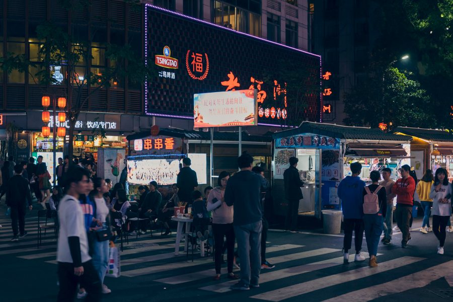 People walking on a street with lit-up storefronts and food stalls in Sanfang Qixiang.