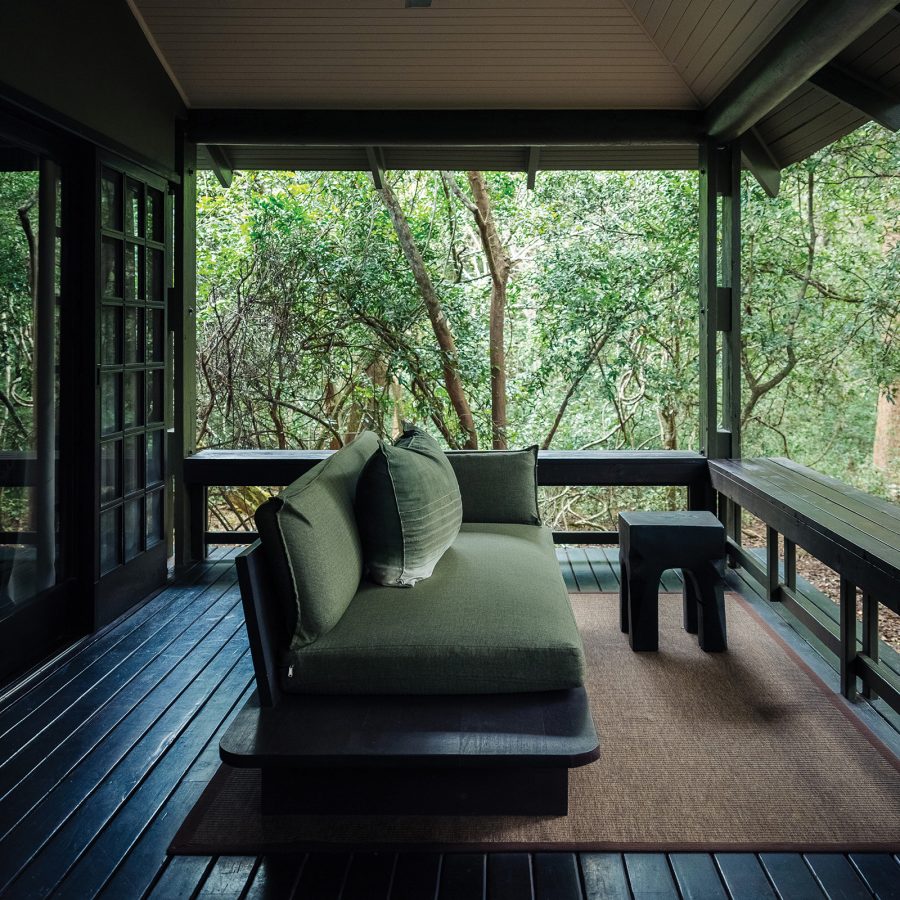 A room’s veranda at Phinda Forest Lodge, with a jute rug and green couch facing into the forest.