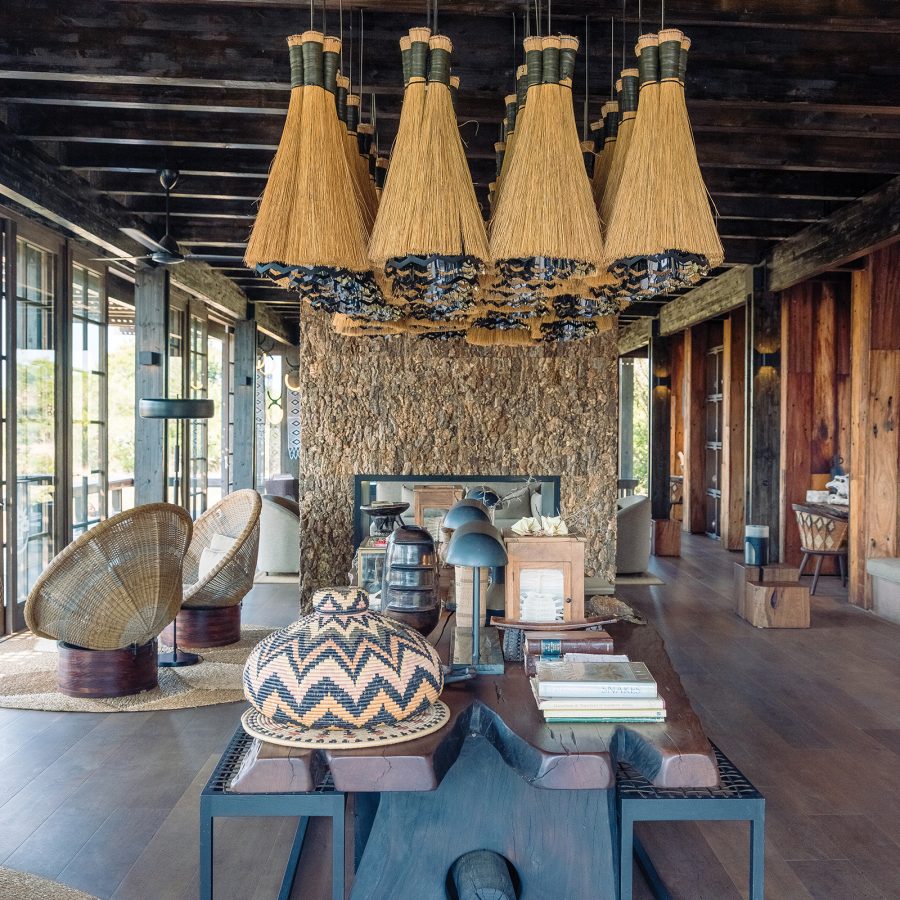 The shared area at Phinda Forest Lodge, showing grass-covered hanging light fixtures and a table with books, art and safari ephemera atop it.