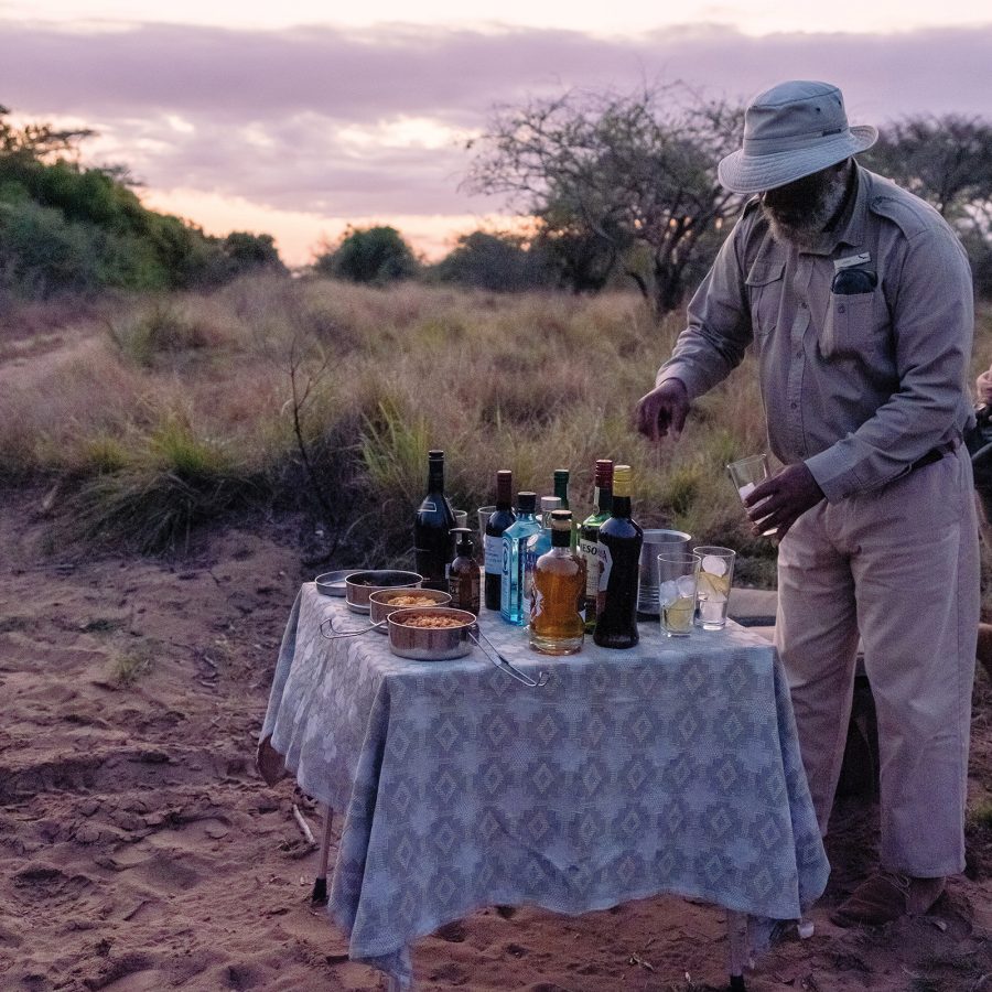 A Phinda tracker lays out drinks and snacks for afternoon tea on a tablecloth-covered table just off the track.