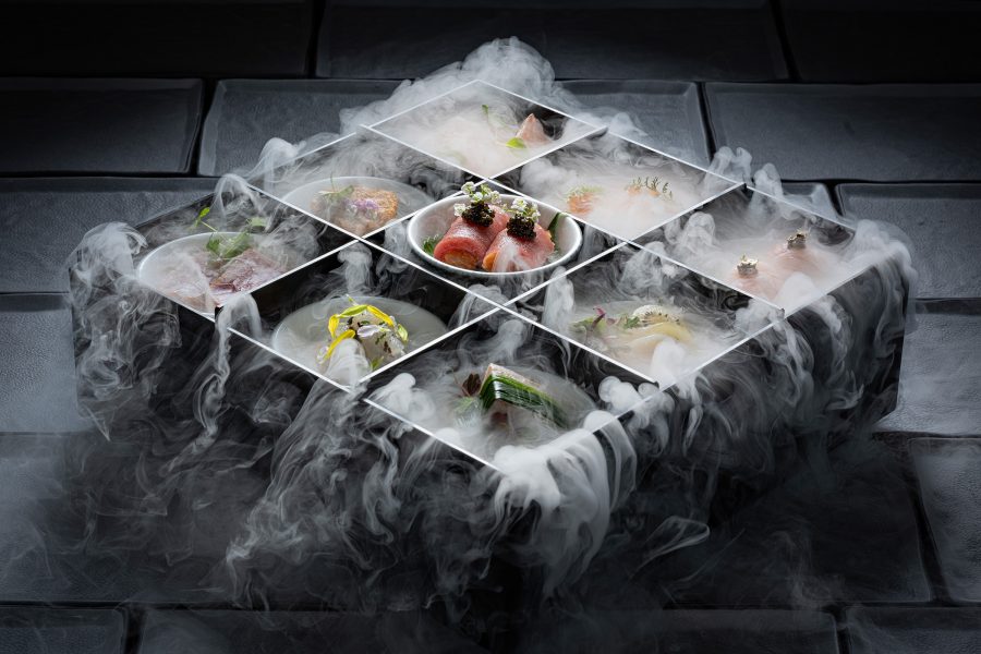 A gridded platter filled with small plates and smoke billowing out over the dishes.