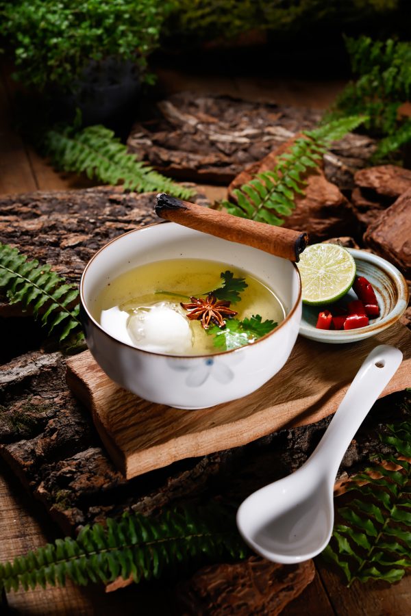 A soup dish in a ceramic bowl laid out on tree bark and leaves.