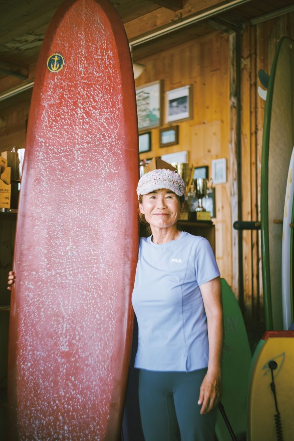 Meehie Seo posing with her surfboard in her shop, Songjeong Surfing Club. 