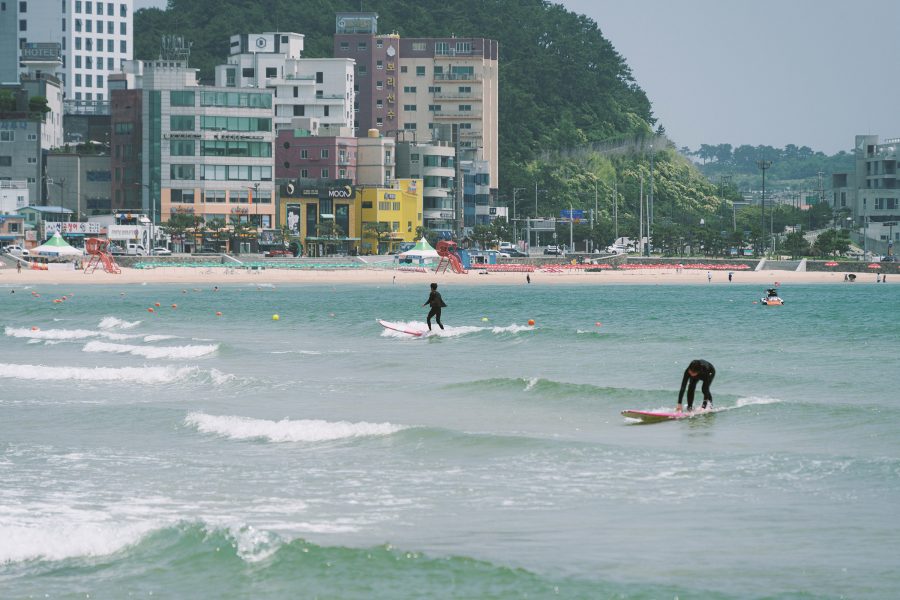Surfers at Busan’s Songjeong Beach, with buildings in the distance.