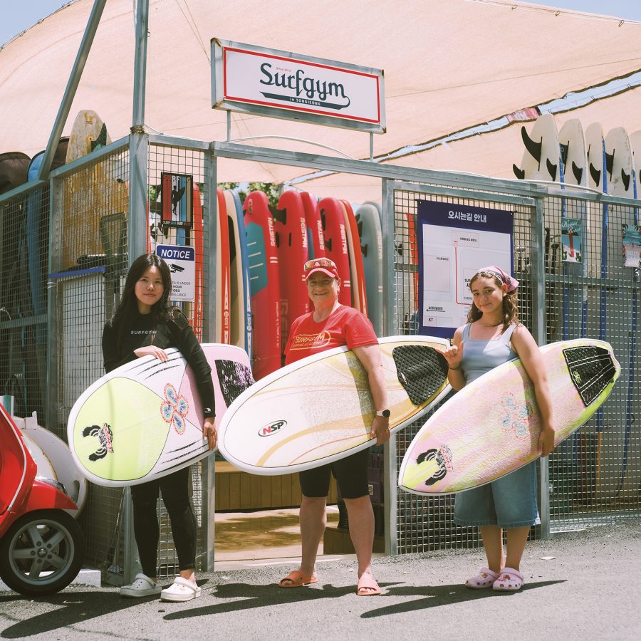 Yujin Park, Cheryl Kim and Kai Kim, holding their surfboards in front of Surfgym’s storage shed.