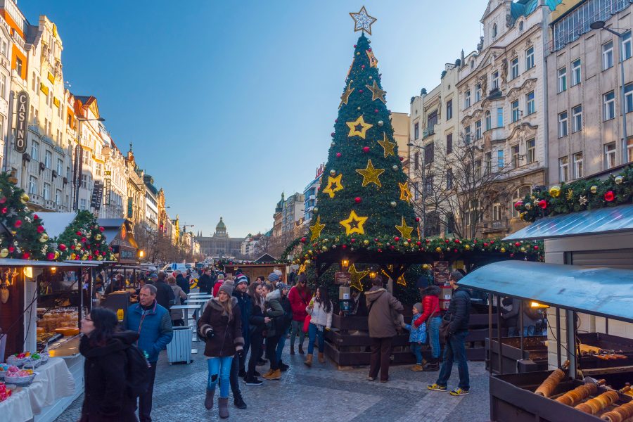 People streaming through the streets at a Prague Christmasmarket with a tree in the background.