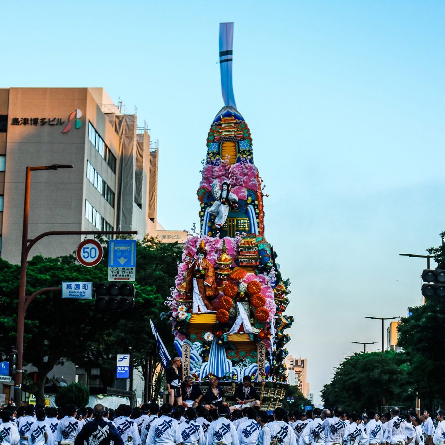 Rows of uniformed participants line up to pay tribute to a towering float on a busy main street in Fukuoka.
