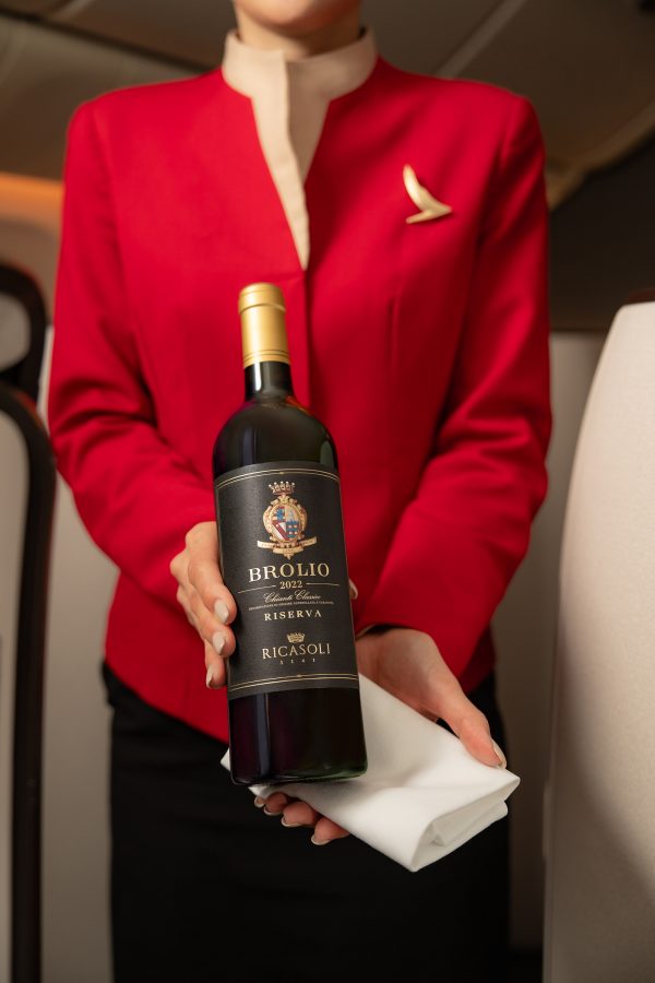A flight attendant in red Cathay Pacific uniform presenting a bottle of Barone Ricasoli Brolio Riserva Chianti Classico, Italy, 2022.