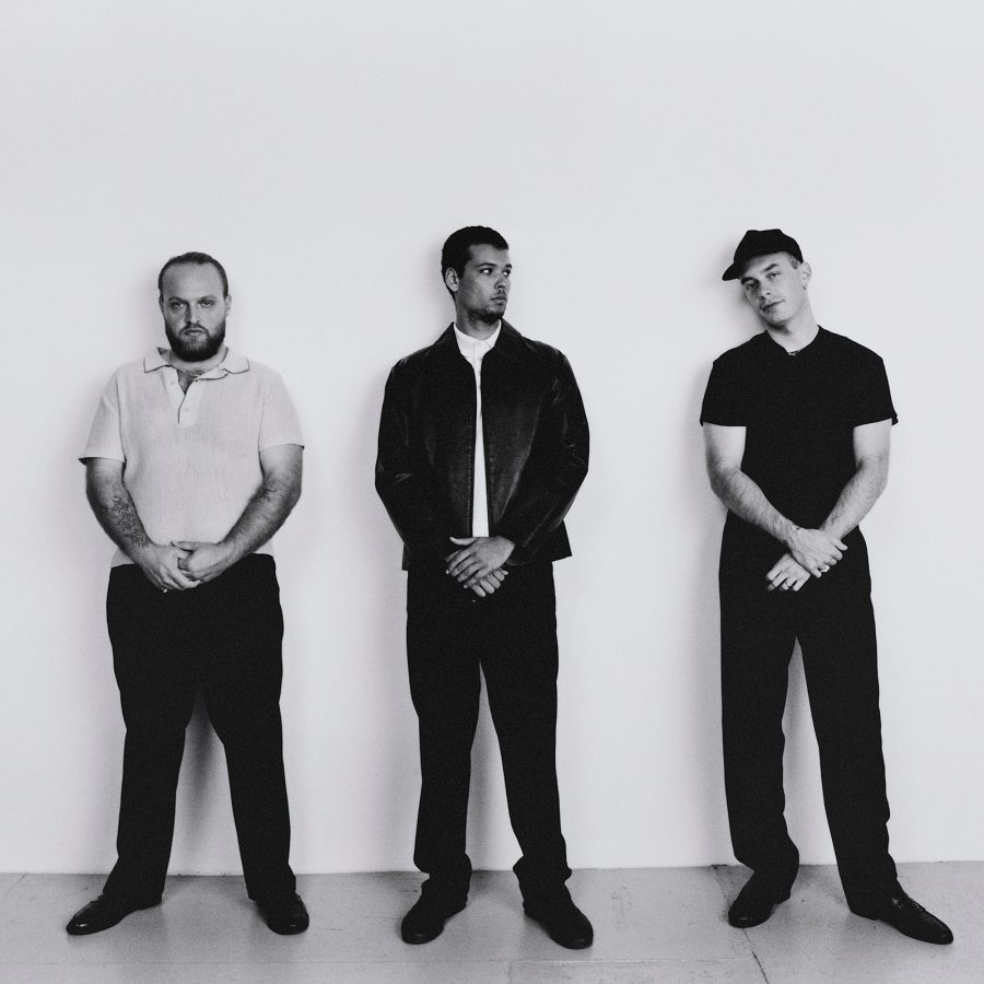 The Moses Yoofee Trio stand against a white wall.