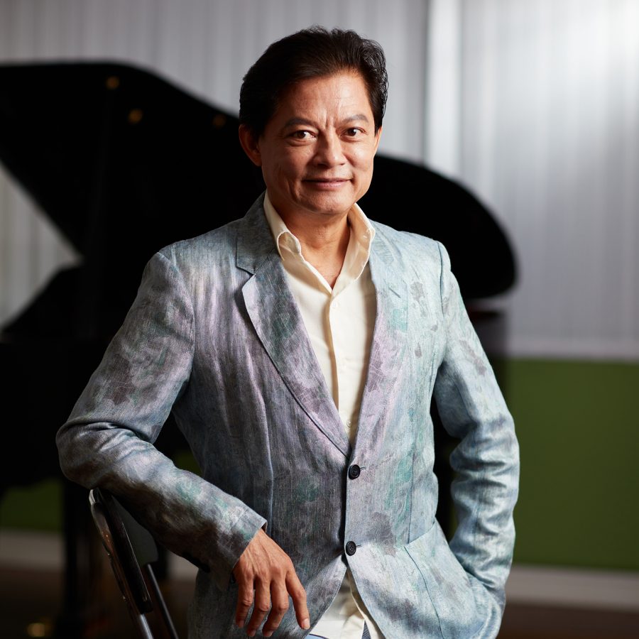 Opera singer Warren Mok sits on a chair for a portrait in a blue suit. 
