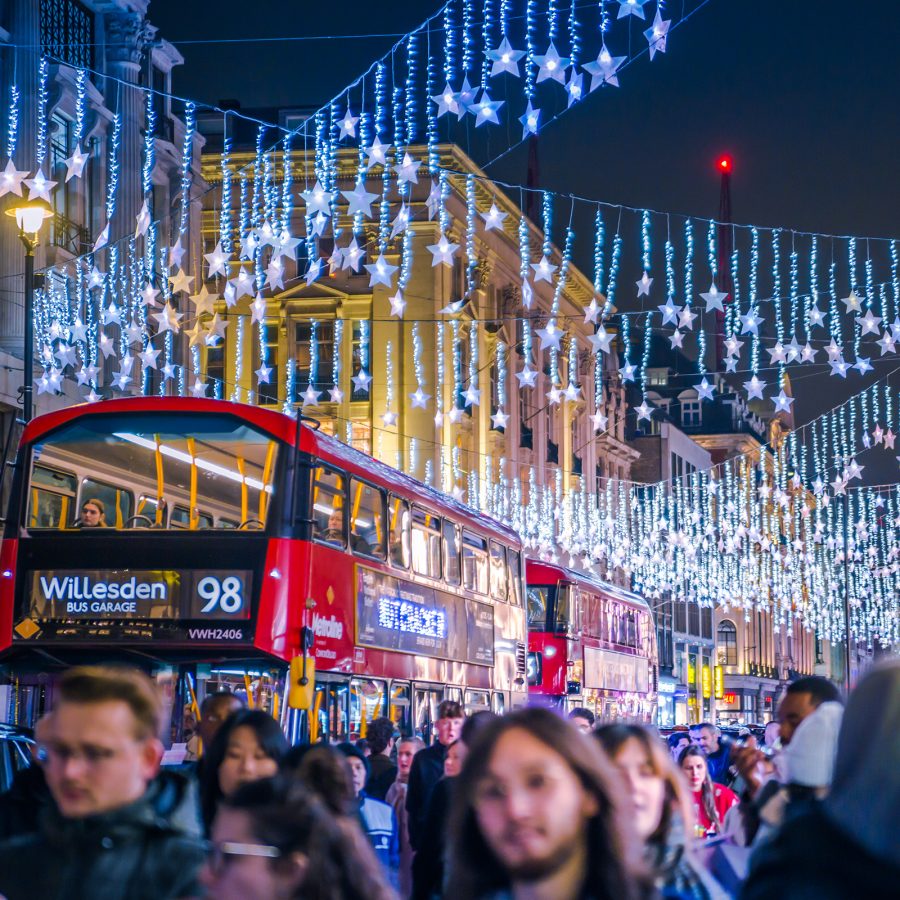 London street decorated with hanging star-shaped Christmas lights, featuring a red double-decker bus and festive crowds.