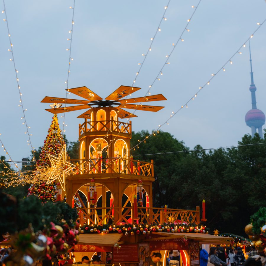 Festive wooden Christmas pavilion decorated with lights at Shanghai Disneyland, with the Oriental Pearl Tower visible in the background.