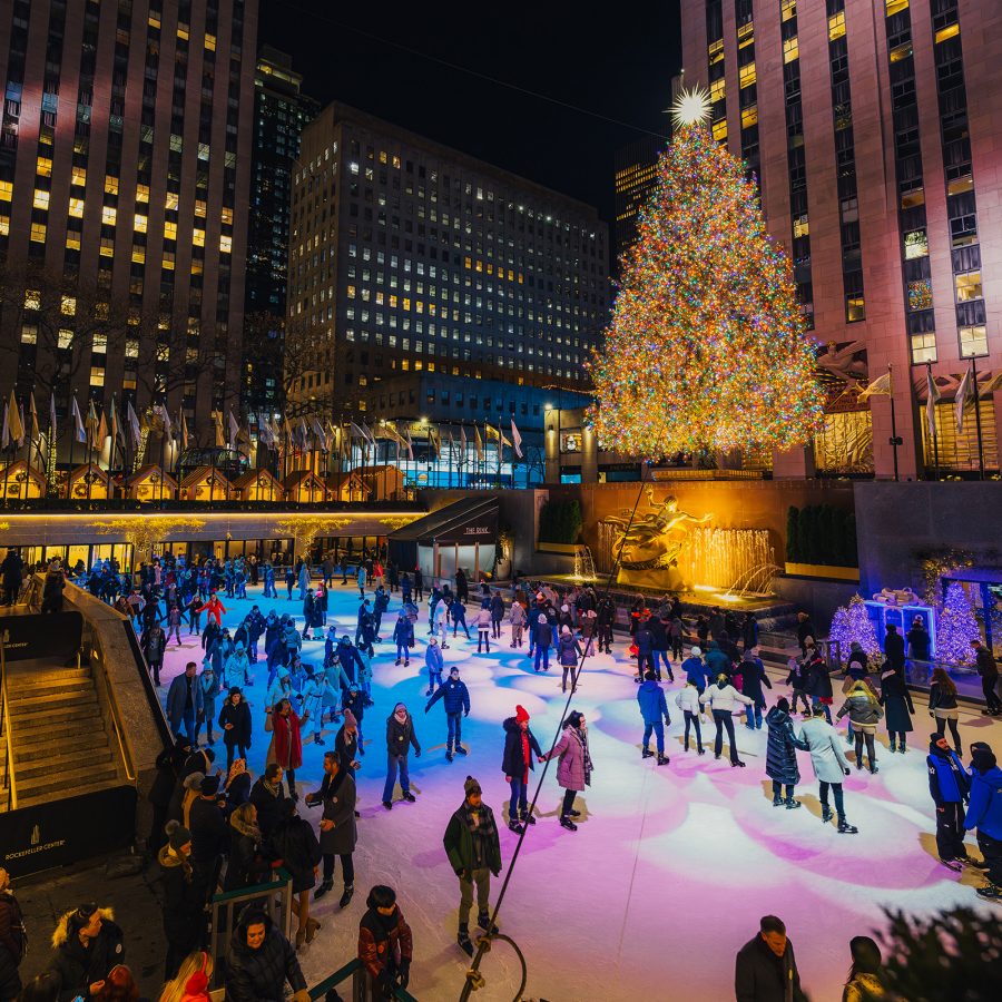 Rockefeller Center ice skating rink at night with a large illuminated Christmas tree and surrounding city buildings.