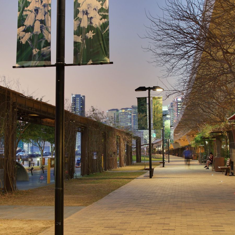 Nighttime view of Kwun Tong promenade featuring a spacious walkway lined with wooden benches, with city buildings illuminated in the distant background.  Credti: Getty Images