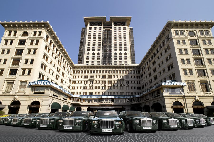 Exterior daytime view of The Peninsula Hong Kong, with a line of Rolls-Royce cars in the driveway. 
