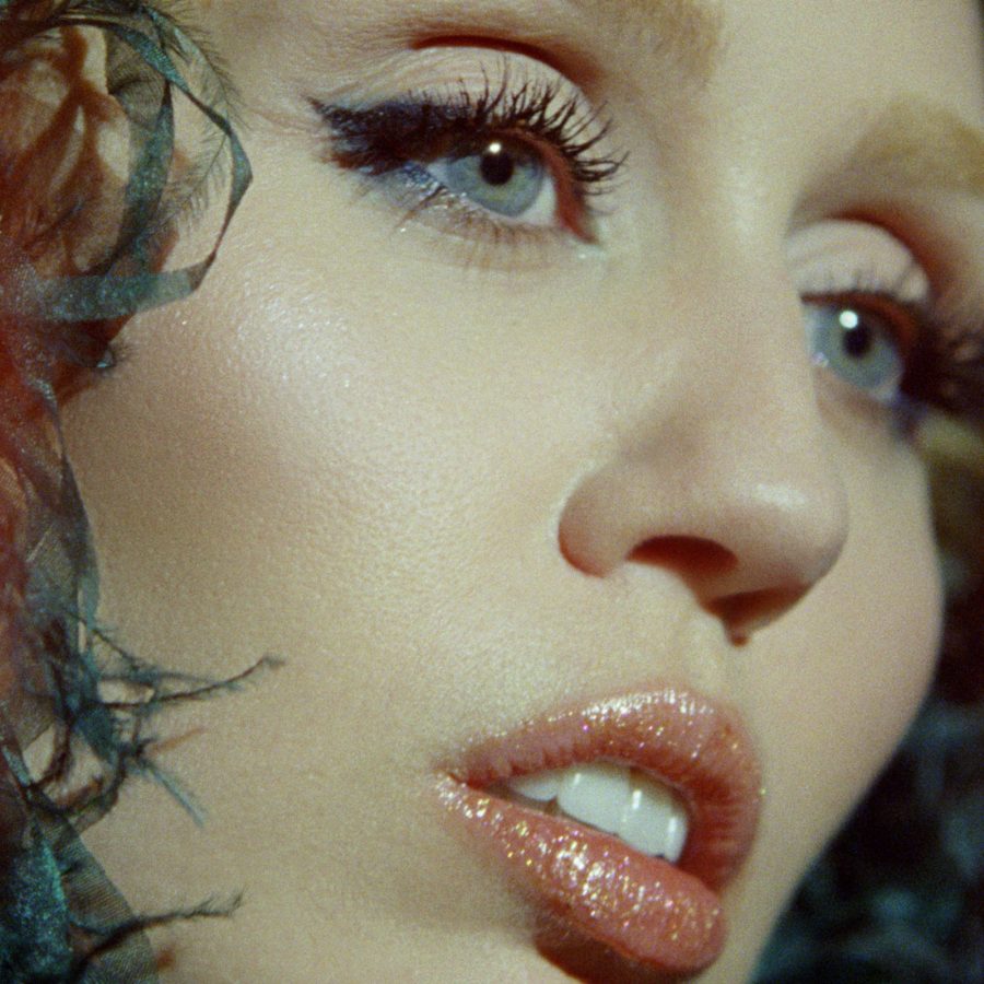 A close-up image of singer Miley Cyrus in a black feathery outfit, from Miley Cyrus: Something Beautiful