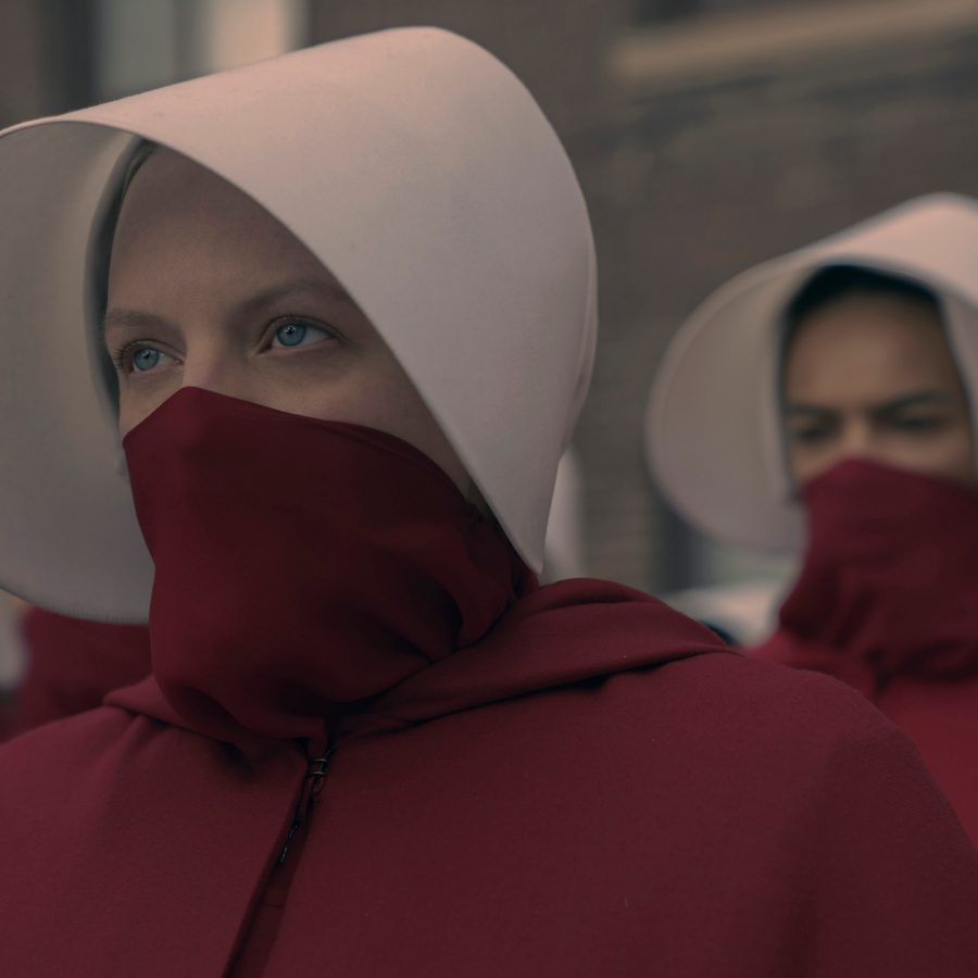 A scene from The Handmaid’s Tale shows a group of women dressed in red cloaks that cover their noses and mouths, and white hats with large hoods