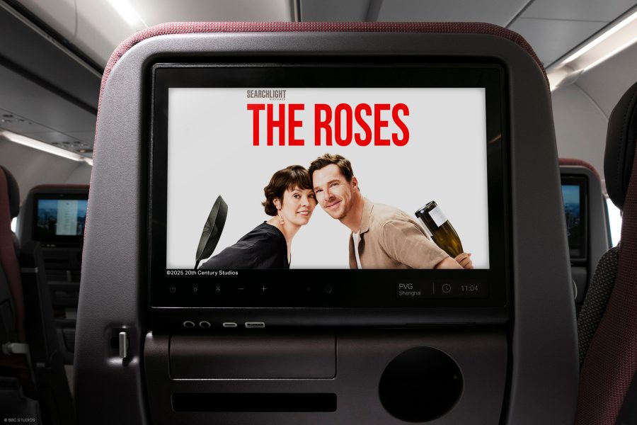 A seatback screen on a Cathay Pacific plane displays a promotional image for The Roses, showing a smiling man and woman hiding weapons behind their backs. 