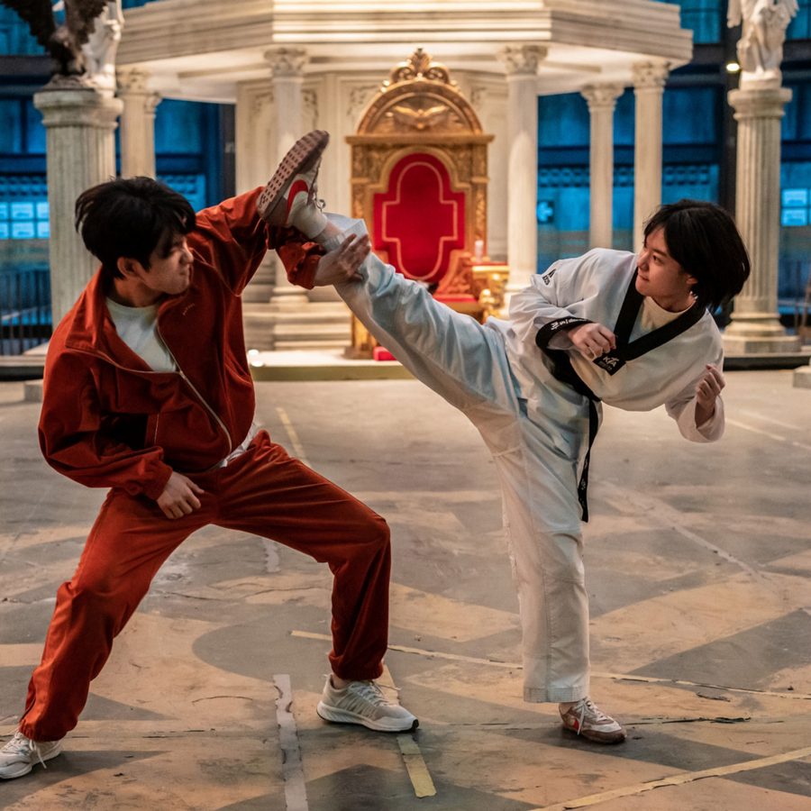 A woman dressed in white and a man dressed in red engage in a martial arts fight in a large opulent room, in a scene from Hi-Five.