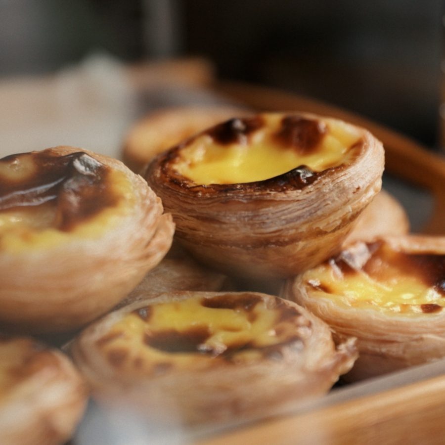 Close-up of Portuguese egg tarts with blistered tops sitting on a wooden tray lined with parchment paper.
