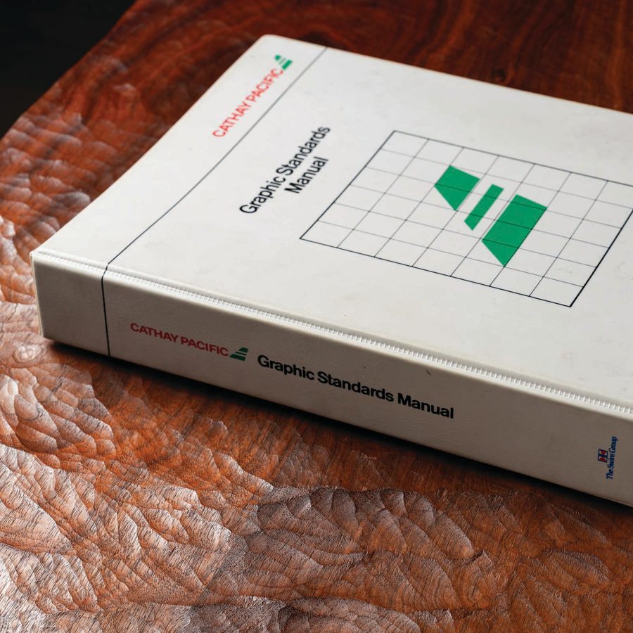 Cathay Pacific Graphic Standards Manual in a white ring binder resting on a wooden tabletop.