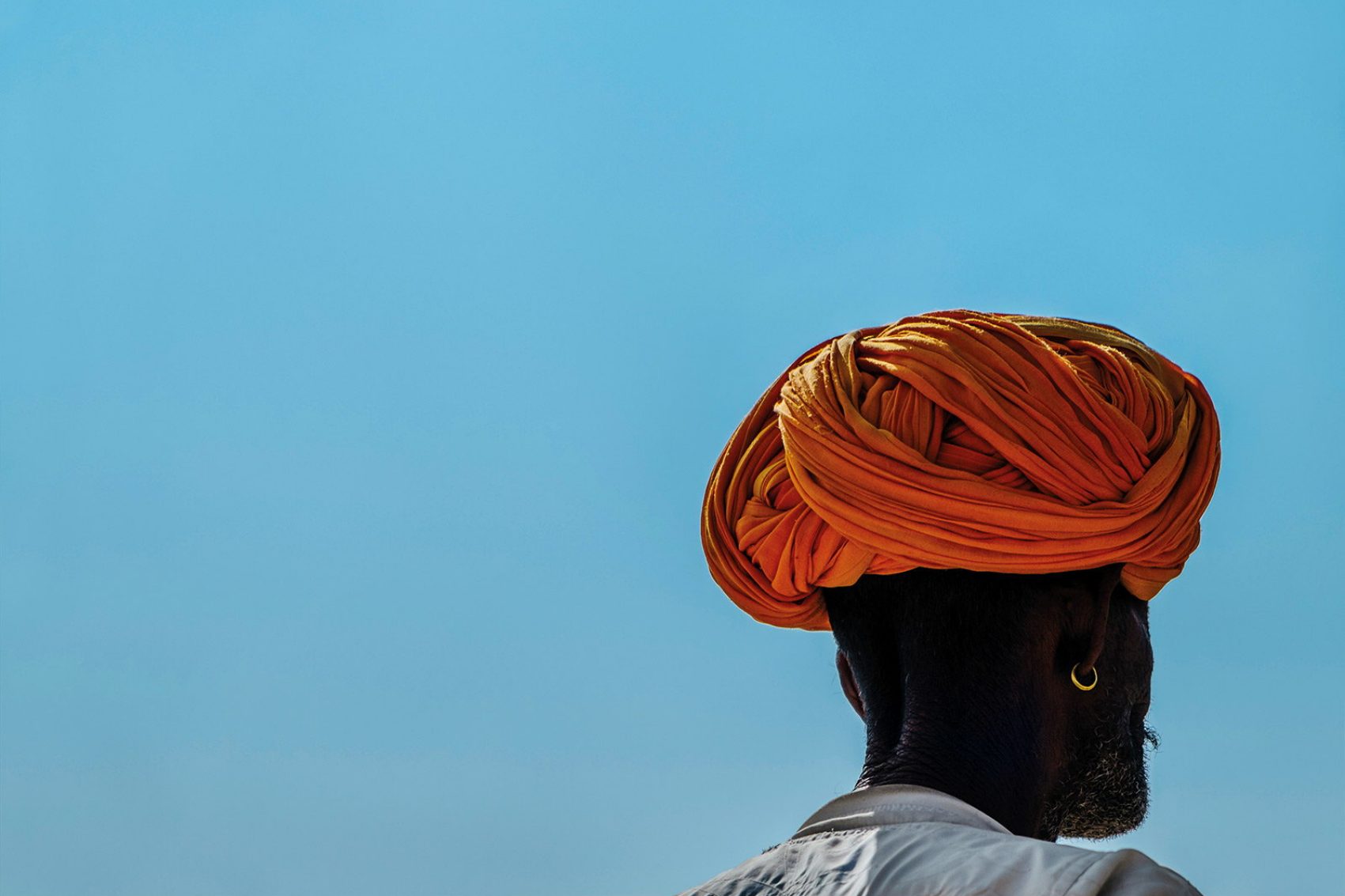 Man wearing bright orange turban in front of bright blue sky