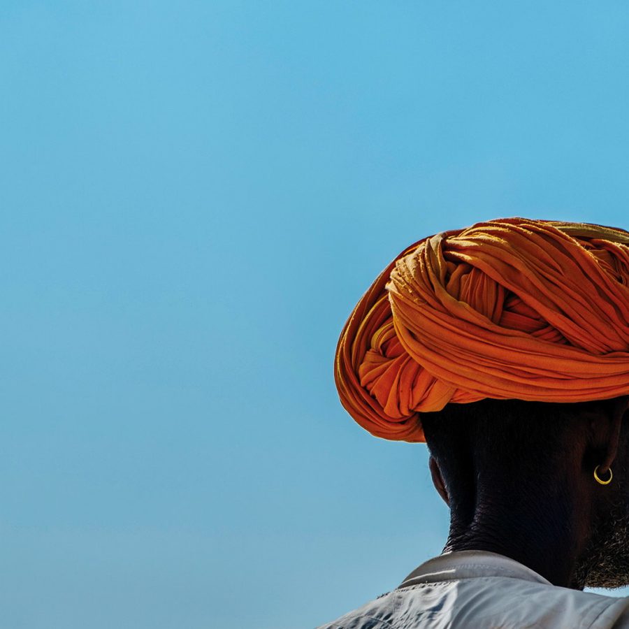 Man wearing bright orange turban in front of bright blue sky