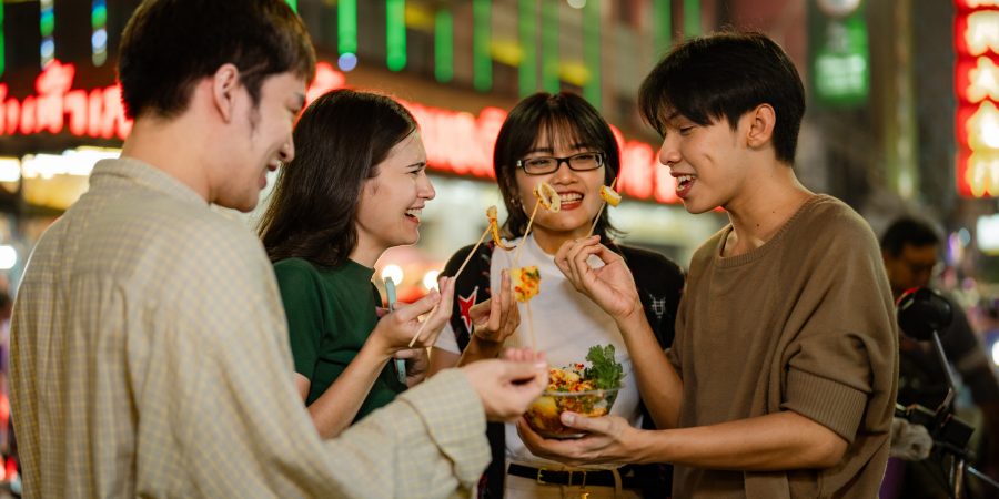 A group of four friends enjoying a snack together, with neon shop signs in the background