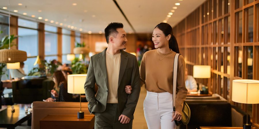 A young Asian couple walking through Cathay Pacific’s airport lounge. Ambient lighting and seating in the background.