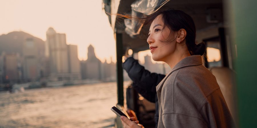 An Asian woman holding a phone looks out across Hong Kong harbour from the Star Ferry.